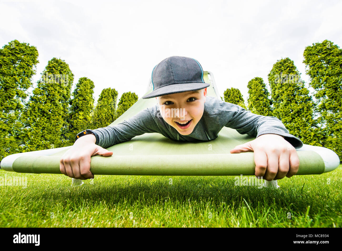 Young boy hanging down on raised hammock chair in the green garden. Stock Photo