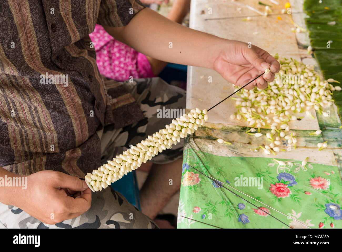 A man threads flower s on to a metal needle to make a decorative flower arrangement in the flower market Bankok Thailand Stock Photo