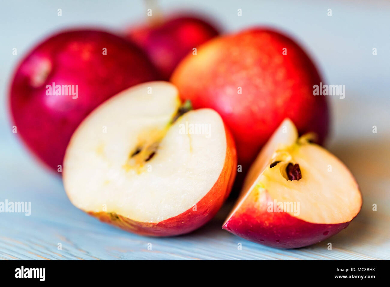 Close up ripe red apples whole and cut in halves in on light blue wooden surface. Selective focus Stock Photo
