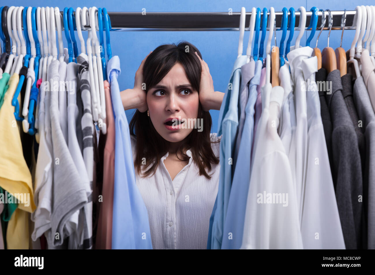 Close-up Of A Stressed Young Woman Standing In Front Of Clothes Rail Stock Photo