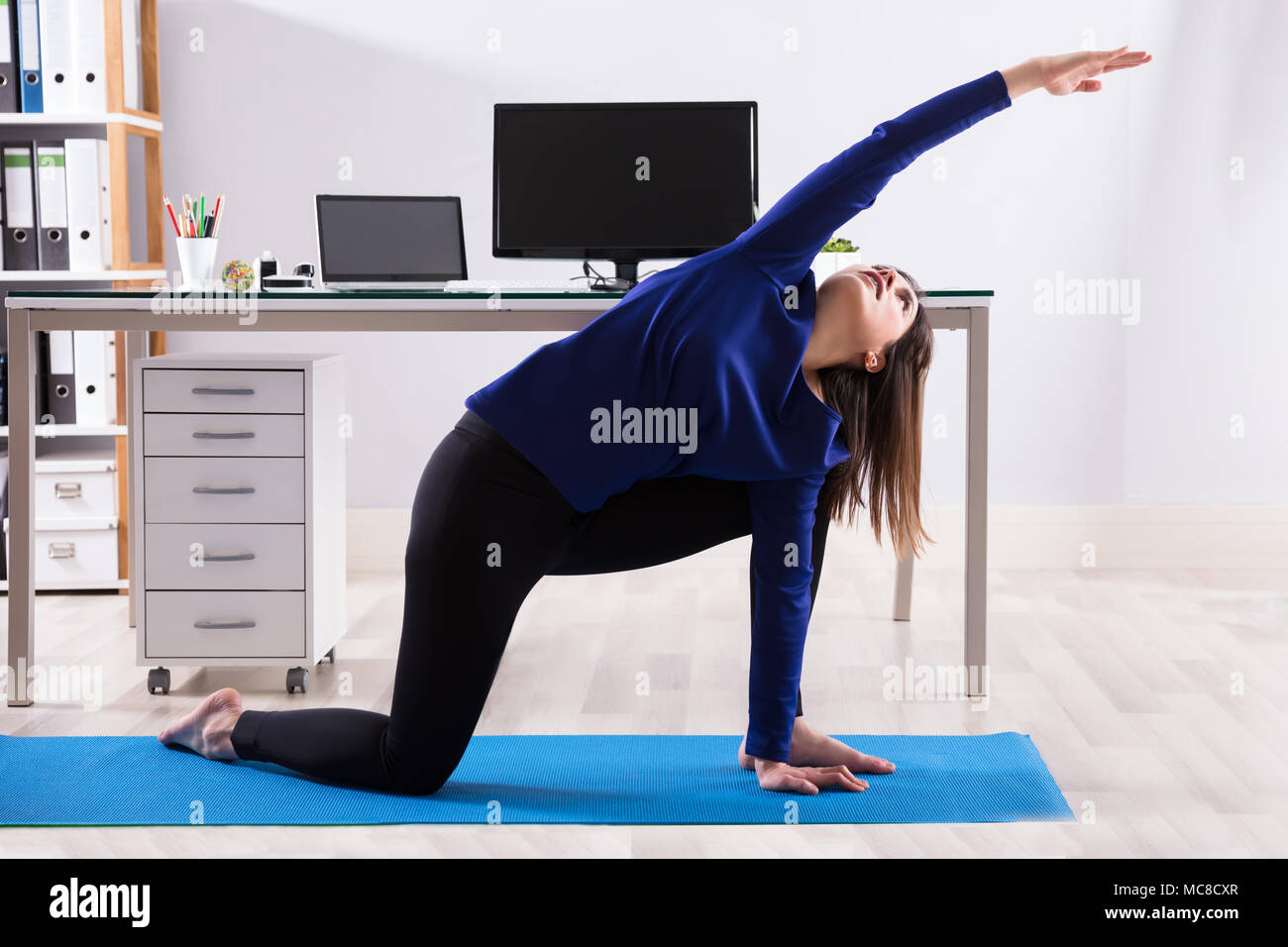 Side View Of A Young Businesswoman Doing Workout On Exercise Mat In Office Stock Photo