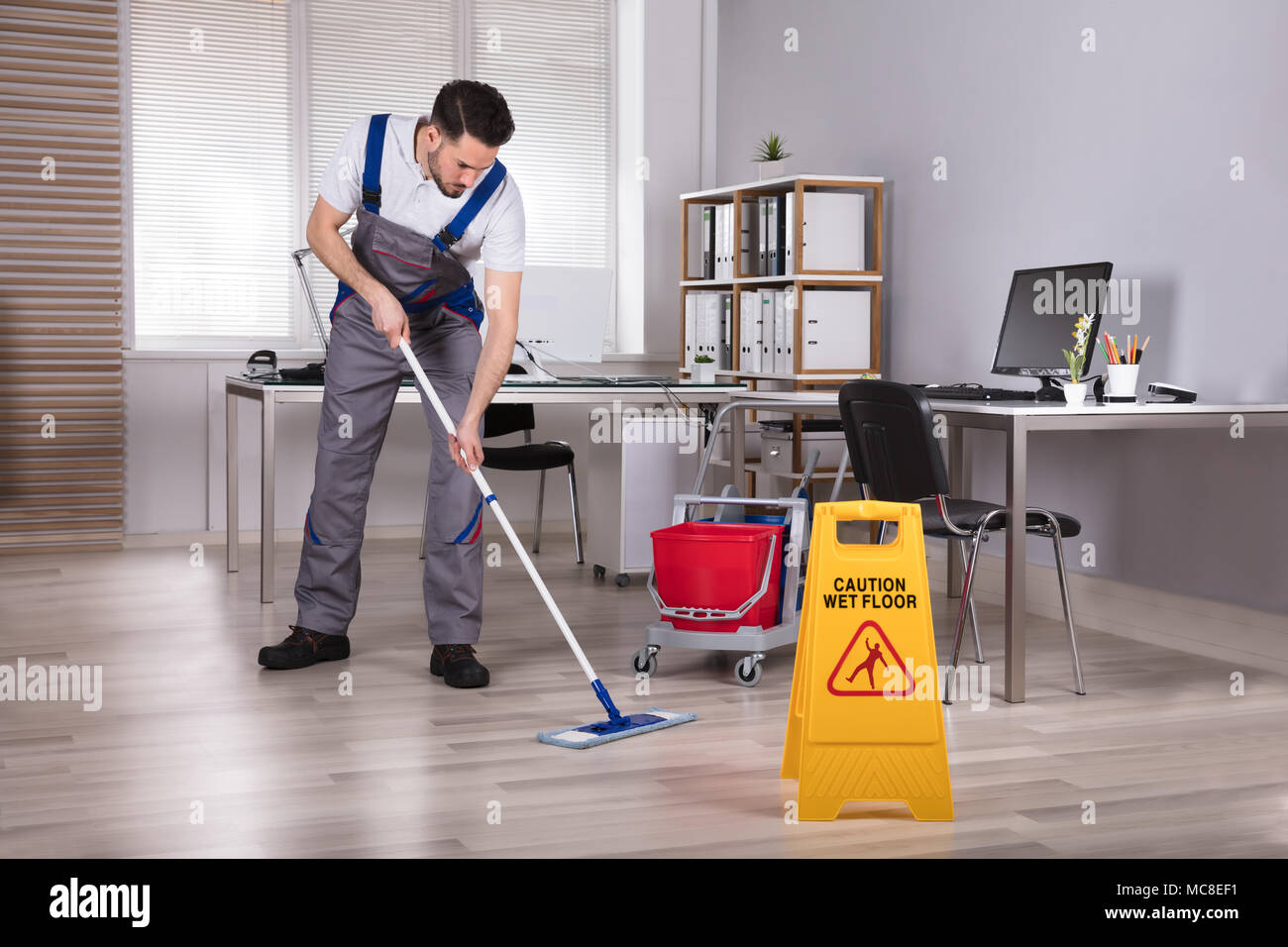 Man Cleaning Office With Mop Near Caution Wet Floor Sign Stock