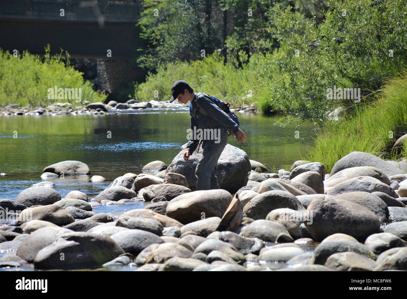 Young boy crosses a calm flowing river to fly fish in Yosemite National Park Stock Photo