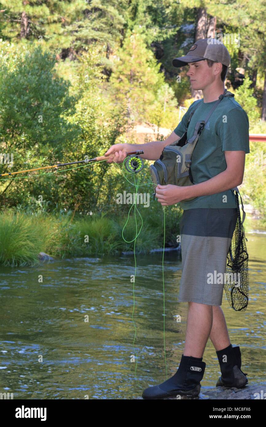 Teen boy enjoys fly fishing in a flowing stream in northern California USA Stock Photo