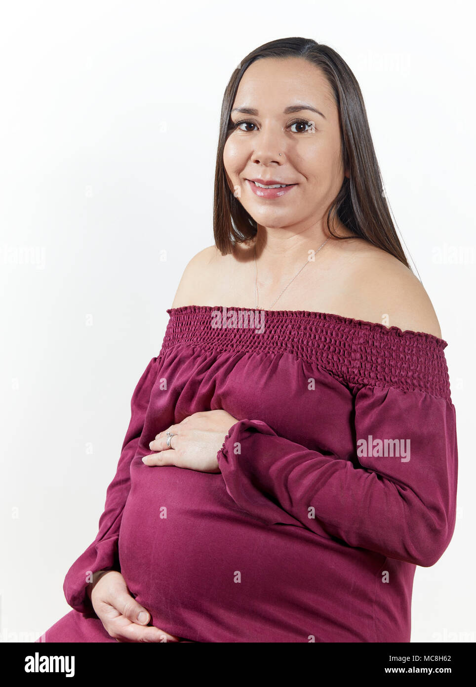 Attractive pregnant woman with her hands on her tummy sitting down isolated on white Stock Photo