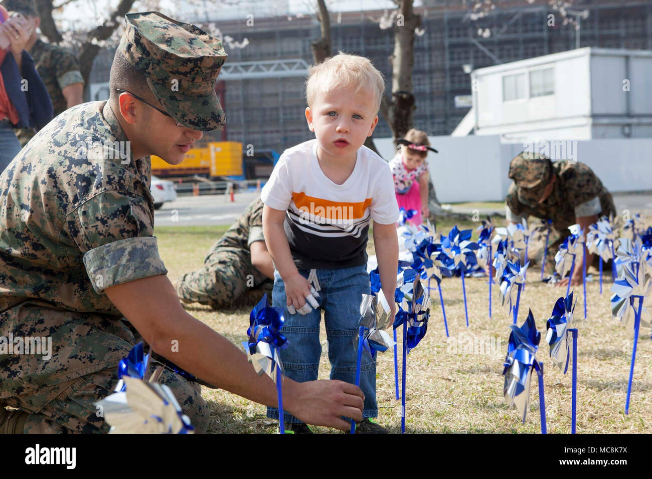 U.S. Marine Corps Lance Cpl. Andre Vianna, motor vehicle operator with Marine Wing Support Squadron (MWSS) 171, helps Jake Katzenberger, Marine Corps Air Station (MCAS) Iwakuni resident, plant blue pinwheels during the 2018 National Child Abuse Prevention Pinwheel Planting at MCAS Iwakuni, Japan, March 29, 2018. The blue pinwheels were planted as a part of the National Child Abuse Prevention Month activities and provide the opportunity for individuals and organizations to take action. Stock Photo