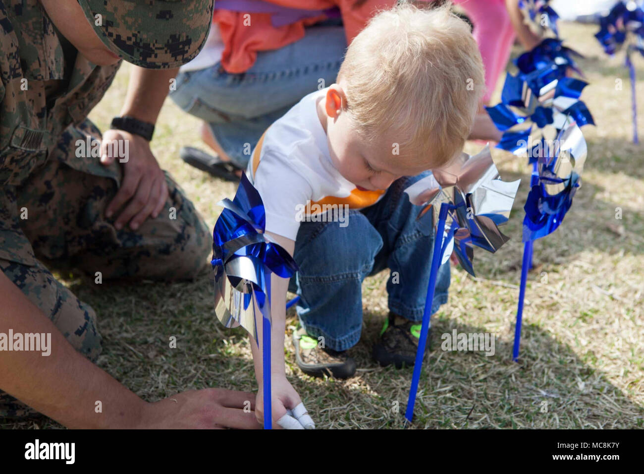 U.S. Marine Corps Lance Cpl. Andre Vianna, motor vehicle operator with Marine Wing Support Squadron (MWSS) 171, helps a child plant blue pinwheels during the 2018 National Child Abuse Prevention Pinwheel Planting at Marine Corps Air Station, Iwakuni, Japan, March 29, 2018. The blue pinwheels were planted as a part of the National Child Abuse Prevention Month activities and provide the opportunity for individuals and organizations to take action. Stock Photo
