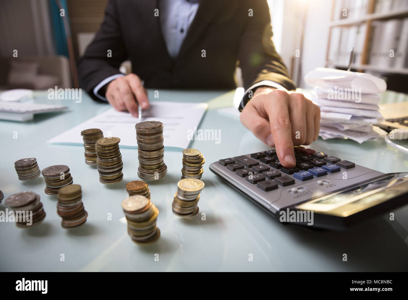 Close-up Of Stacked Coins In Front Of Businessman Working On Document ...