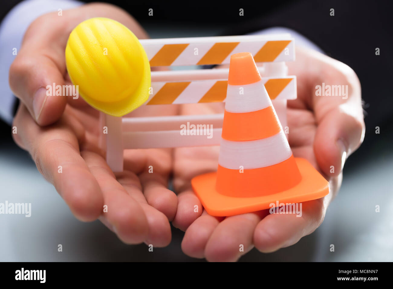 Close-up Of Person's Hand Holding Barricade With Traffic Cone And Hard Hat Stock Photo