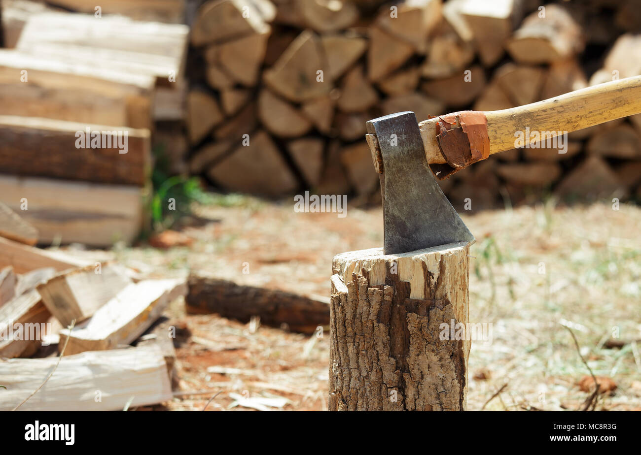 Axe in a stump near the stack of chopped firewood logs. Wood splitting. Close-up. Stock Photo