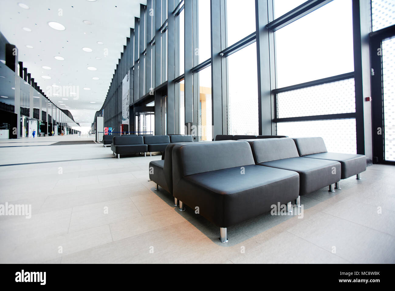 Long aisle inside modern airport lounge with several black leather seats along Stock Photo