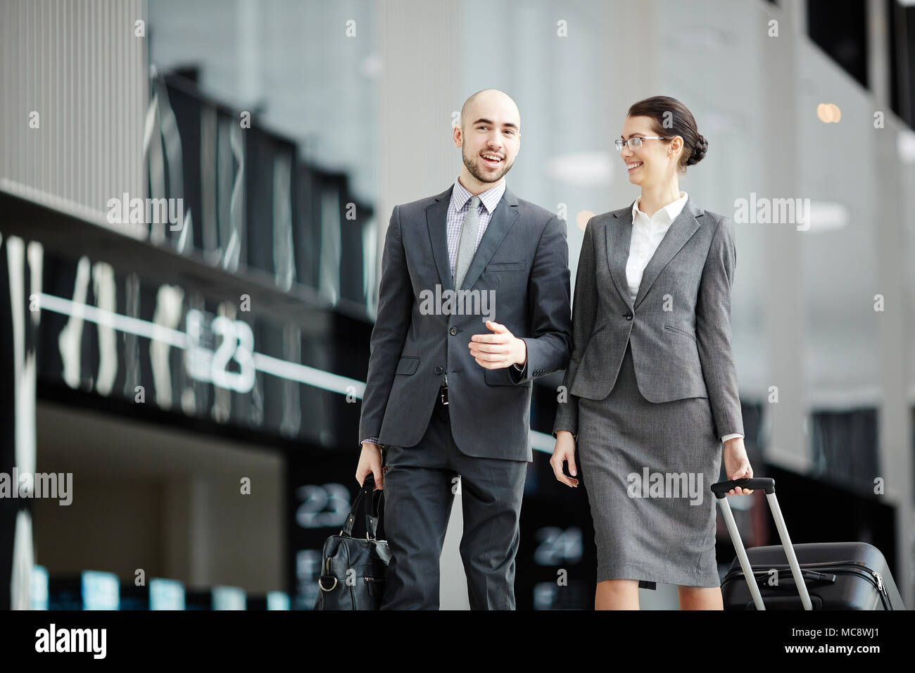 Young business travelers with baggage having talk while walking to