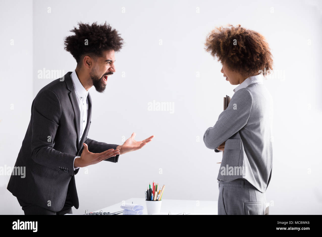 Angry Young Businessman Shouting At Female Executive In Office Stock Photo