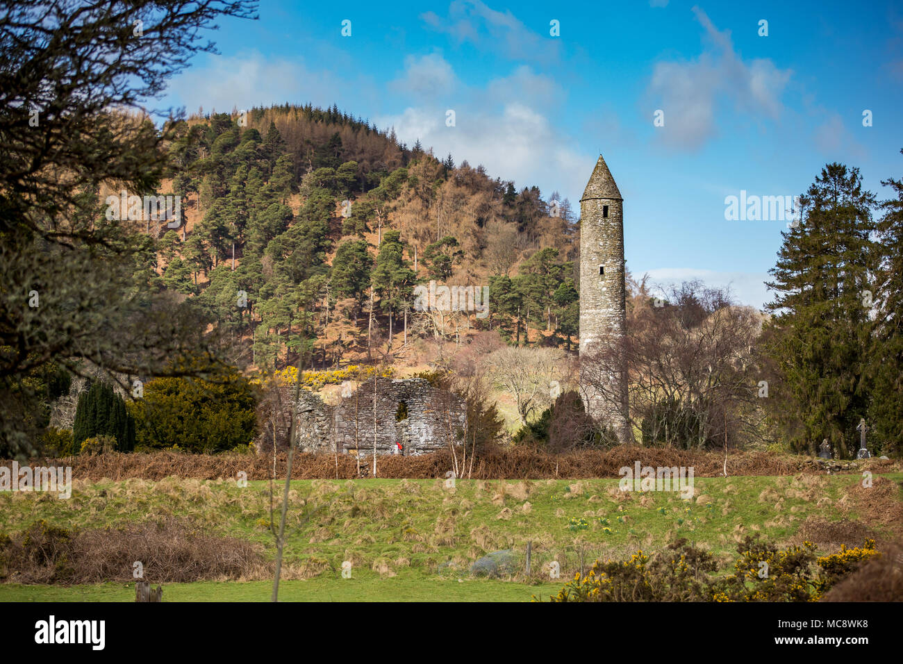 Stone round tower and some ruins of a monastic settlement originally built in the 6th century in Glendalough valley, County Wicklow, Ireland Stock Photo