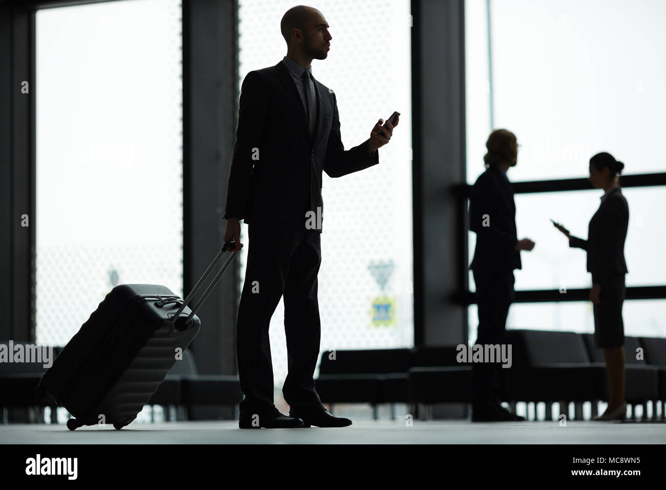 Young businessman with smartphone and suitcase waiting for announcement of his flight in airport lounge Stock Photo