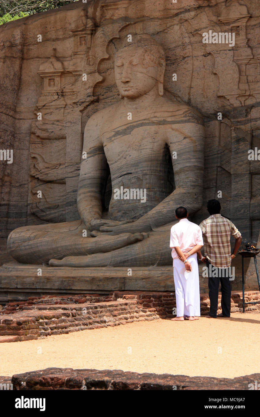 Two Indian or Sri Lankan men in front of a giant Sitting Buddha statue in the royal ancient city of Polonnaruwa in Sri Lanka Stock Photo