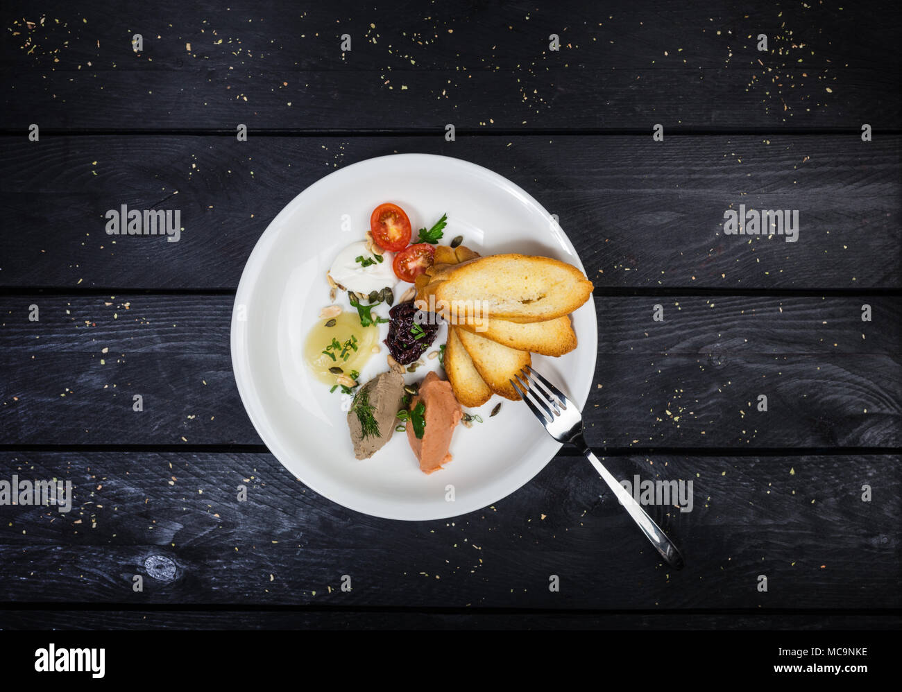 Assorted pates with fried bruschetta served on the white plate with fork on the wooden background. Top view. Stock Photo