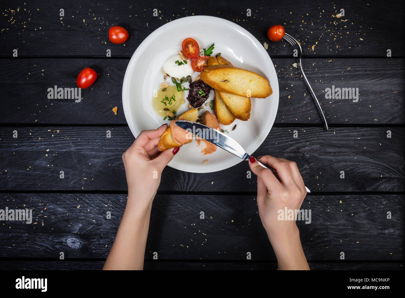 Assorted pates with fried bruschetta served on the white plate with cutlery and hands on the wooden background. Top view. Stock Photo