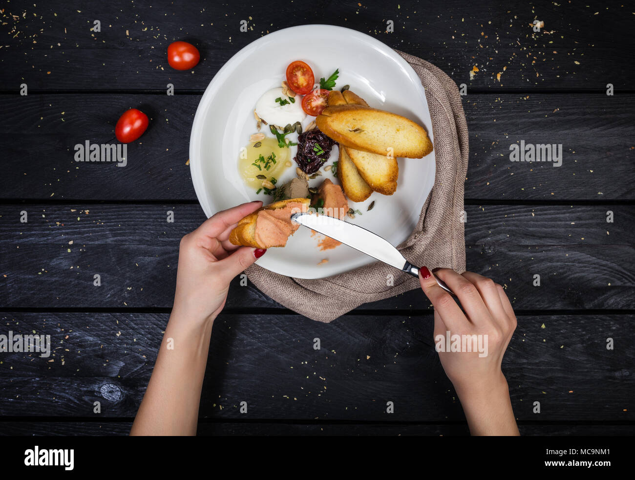 Assorted pates with fried bruschetta served on the white plate with cutlery, linen napkin and hands on the wooden background. Top view. Stock Photo