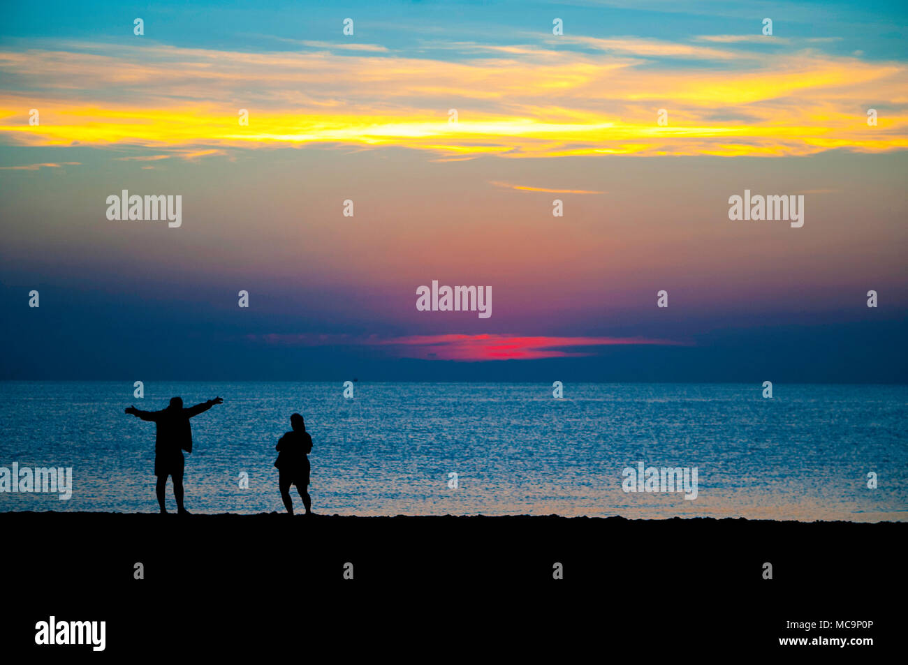 A couple of people silhouetted against the morning Florida Sunrise at the beach. Stock Photo