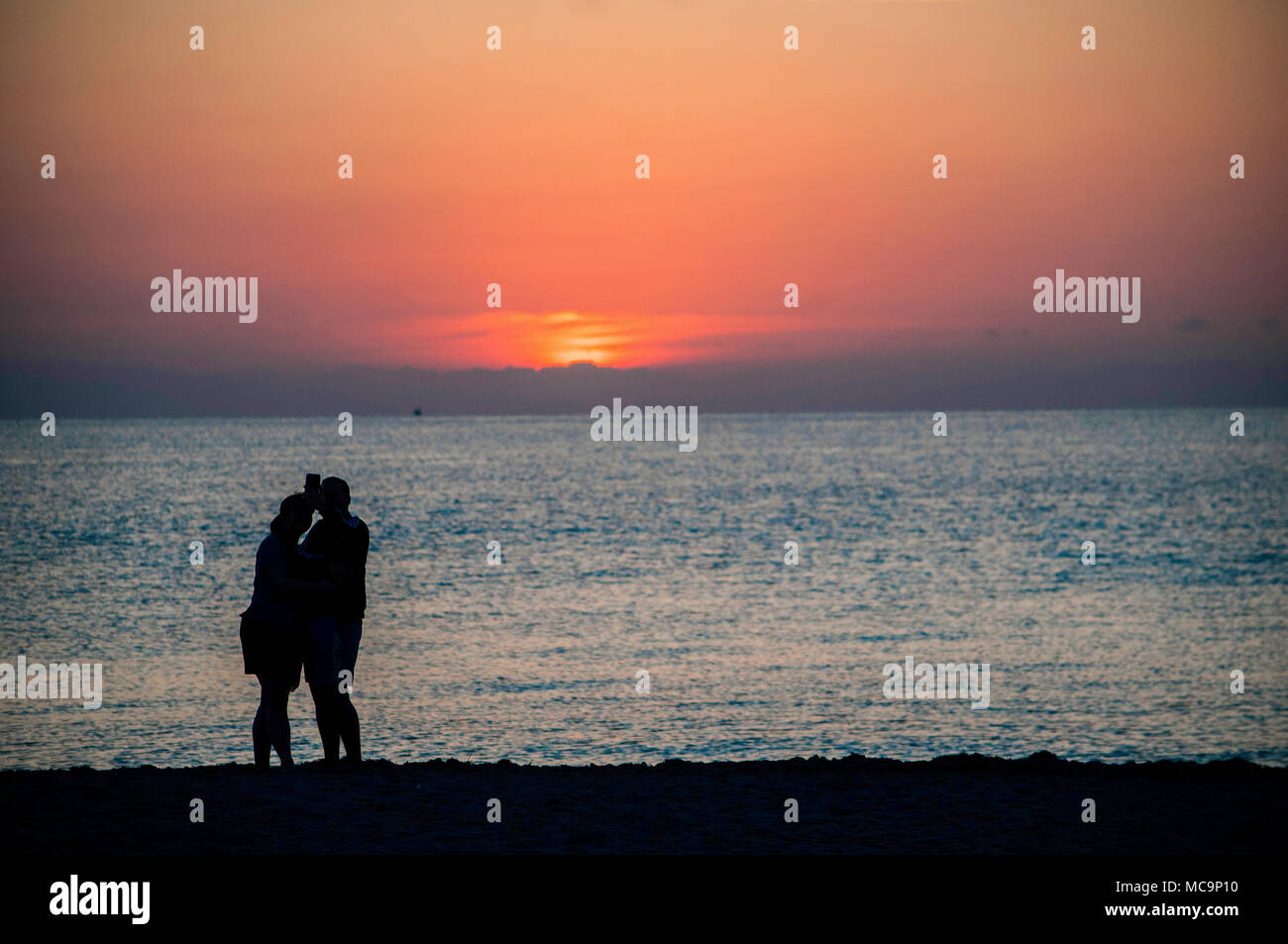 A couple of people silhouetted against the morning Florida Sunrise at the beach. Stock Photo