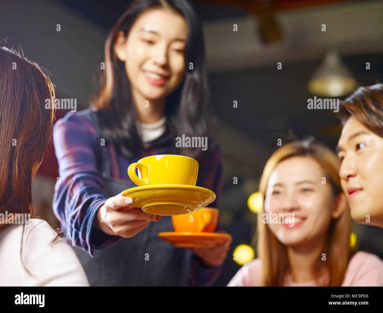 young smiling asian waitress serving coffee to customers, focus on the cup. Stock Photo