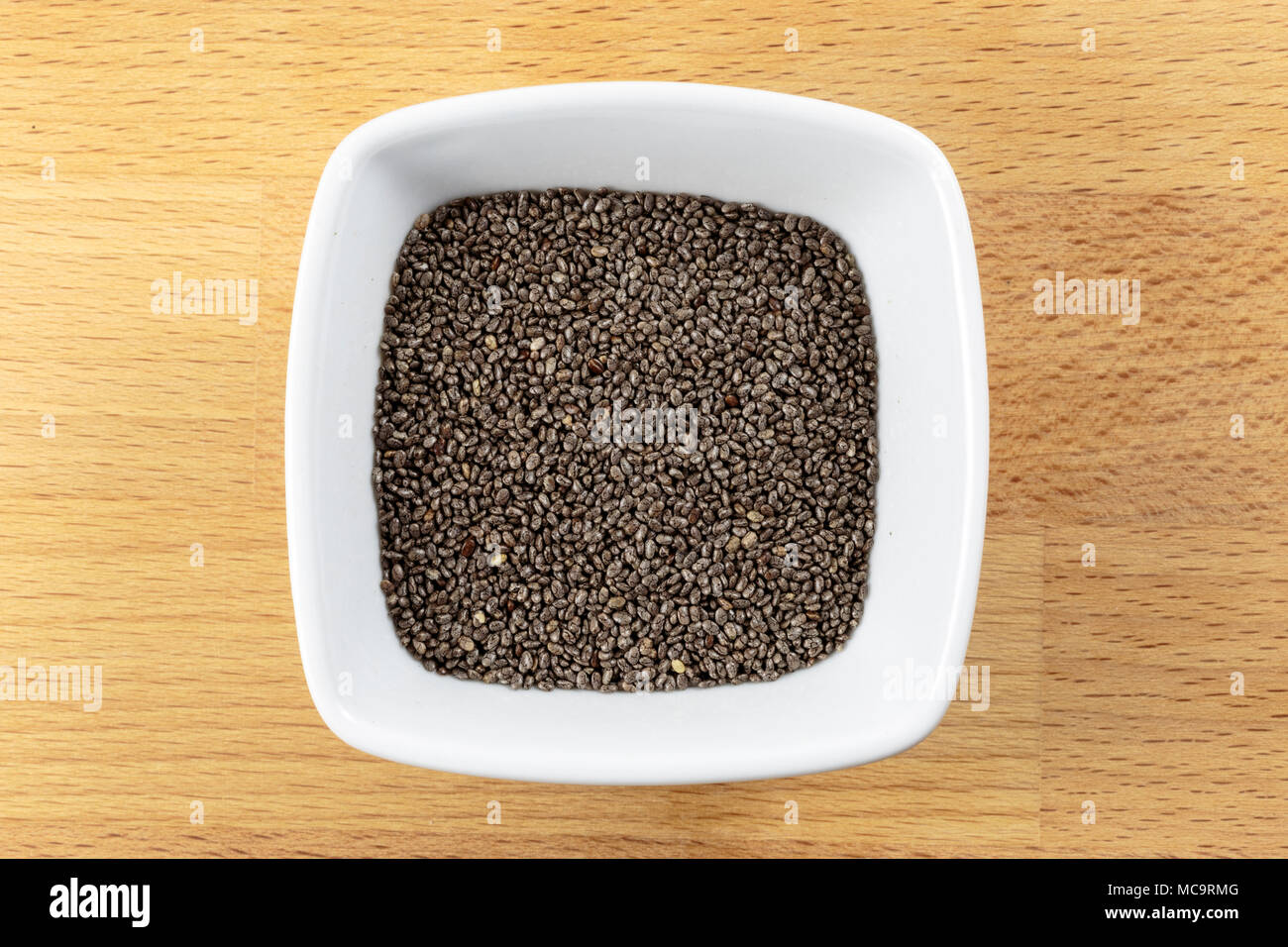 Overhead shot of raw chia seeds in a white bowl on a wooden chopping board background. Chia seed is obtained from Salvia hispanica of the Lamiaceae fa Stock Photo