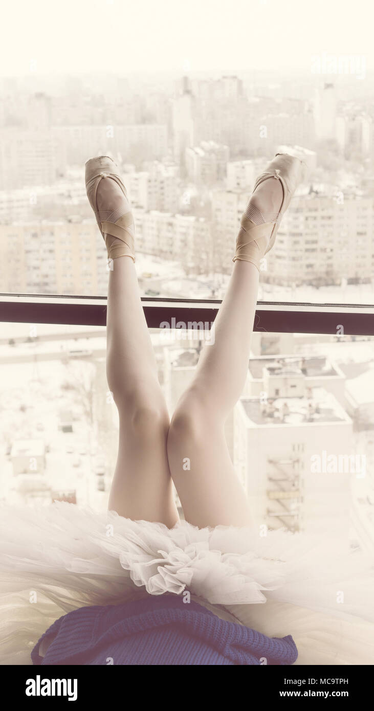 Slender ballerina feet in pointe shoes. She is lying by window with her legs up Stock Photo