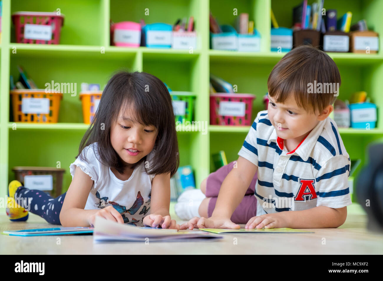 Two kid lay down on floor and reading tale book in preschool library