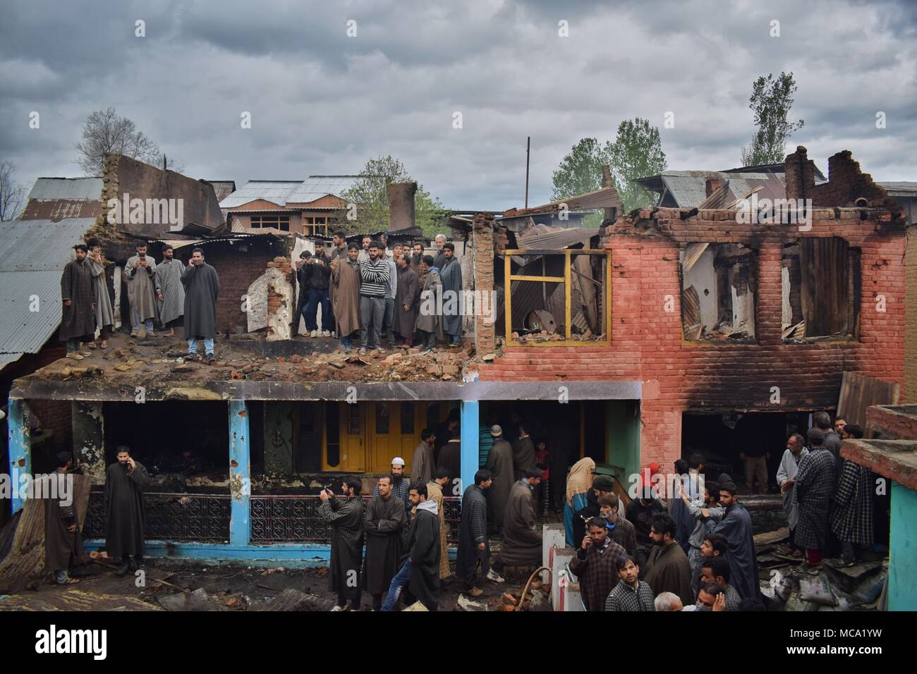 Locals gather near debris of Houses that were destroyed in a Gunbattle between forces and pro-freedom rebels in Khudwani area of South Kashmir's district Kulgam on 11 April 2018. Four Civilians and 1 army man were killed and about 150 civilians were injured in clashes while 3 Rebels escaped by taking advantage of huge crowd assembled near encounter site Stock Photo