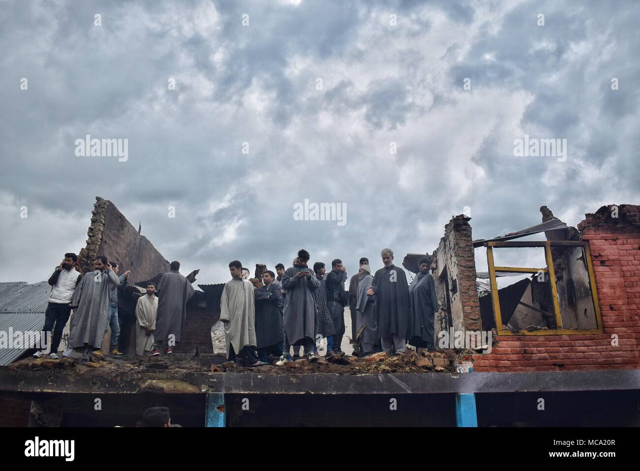 Locals gather near debris of Houses that were destroyed in a Gunbattle between forces and pro-freedom rebels in Khudwani area of South Kashmir's district Kulgam on 11 April 2018. Four Civilians and 1 army man were killed and about 150 civilians were injured in clashes while 3 Rebels escaped by taking advantage of huge crowd assembled near encounter site Stock Photo