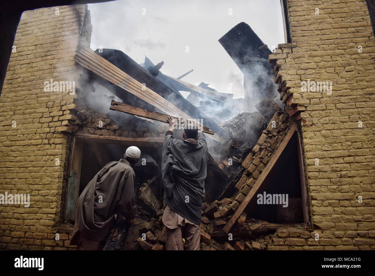 Locals clearing burning things from Houses that were destroyed by Indian forces in a Gunbattle at Khudwani area of South Kashmir's district Kulgam on 11 April 2018. Four Civilians and 1 army man were killed and about 150 civilians were injured in clashes during encounter Stock Photo