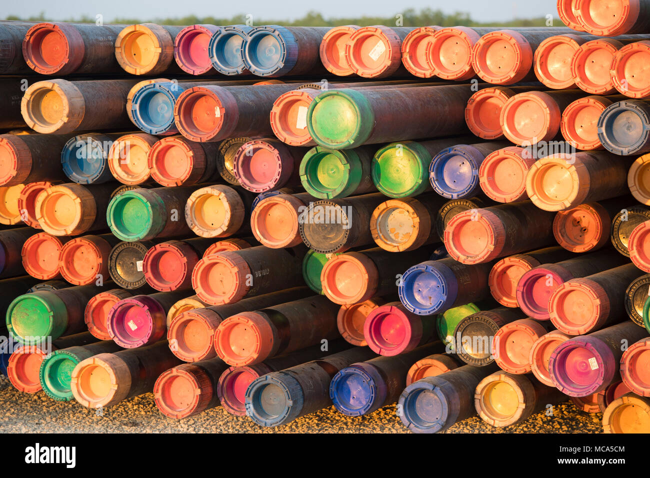 Drilling pipe with colored end caps sit stacked in a yard off Highway
