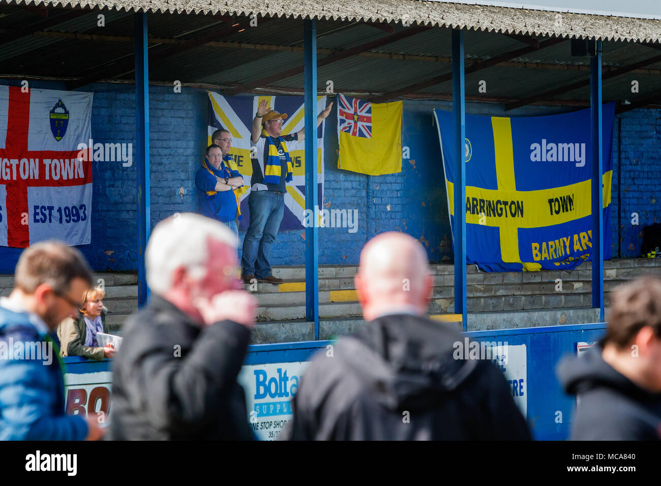 Three Warrington Town supporters stand in front of their flags behind the goal at Throstle Nest, Farsley during the match between Warrington Town FC and Farsley Celtic on 14 April 2018 where Warrington won 2 - 0 Credit: John Hopkins/Alamy Live News Stock Photo
