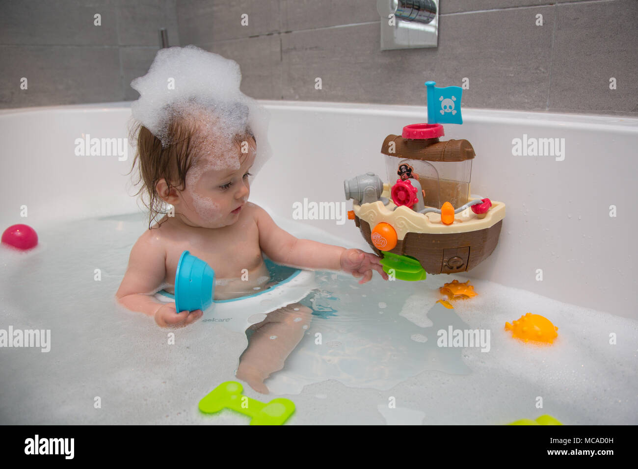 10 month old baby girl having a bath with bubbles on her head Stock