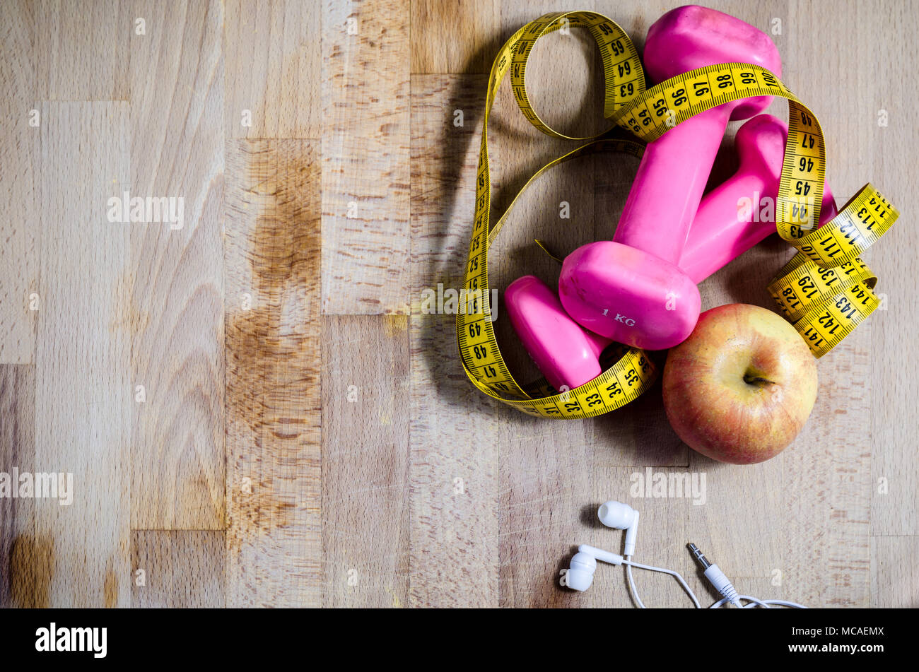 still life with pink weights and  yellow tape measure and an apple from above point of view. fitness. sport. concept. copy space on the left Stock Photo