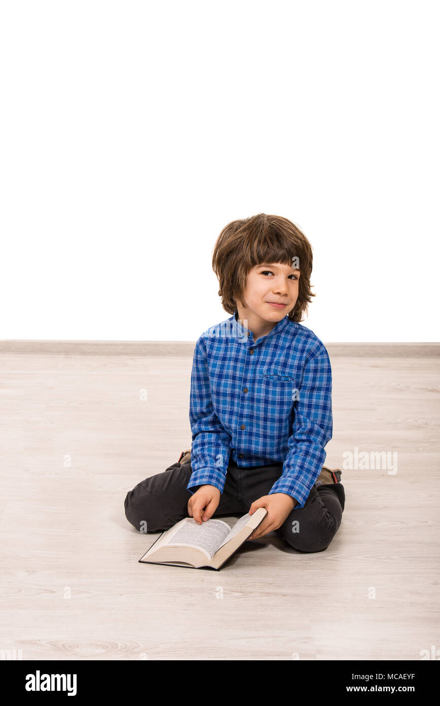 Smiling little cute boy sitting on floor and reading book Stock Photo ...