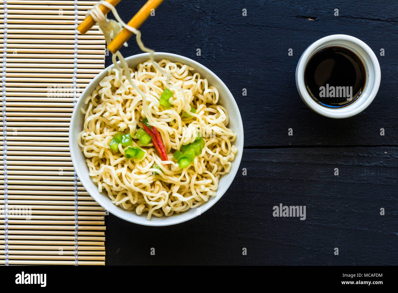 Bowl of instant cooked plain noodles with chopsticks and pepper garnish