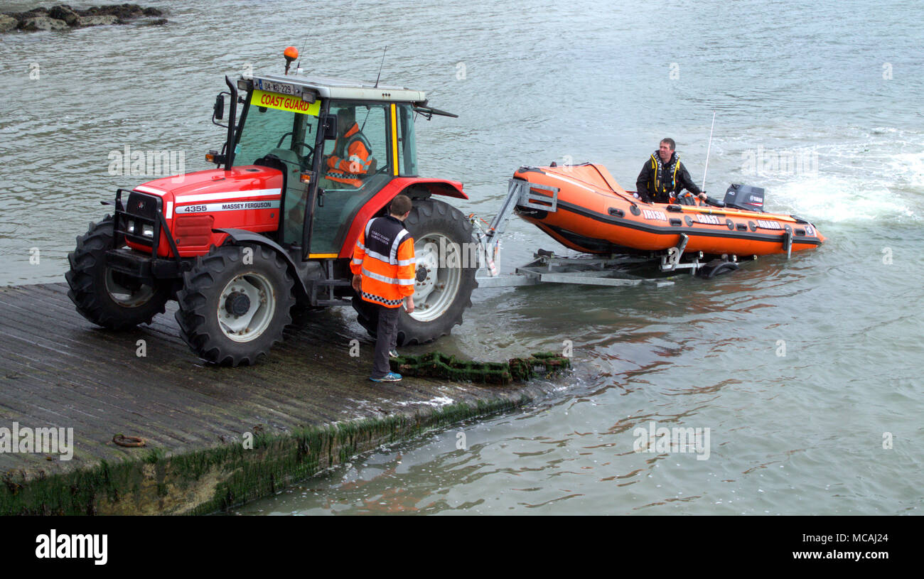 irish coast guard landing their small inshore lifeboat onto a trailer and being hauled up the slipway by a massey ferguson tractor. Stock Photo