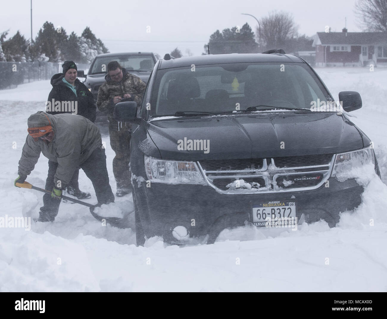 April 14, 2018 - DJ Bromlich, foreground, attempts to help free a Dodge Journey SUV that got stuck in a snowdrift owned by Shelby Buechel, background right, as her friend Kaylin Riser, background left, looks on in Valentine, Nebr. on Sat., April 14, 2018. A historic late season blizzard struck the Northern Plains Friday and Saturday with storm total accumulations ranging from 1-2 feet and sustained winds of 35-45 mph with gusts in excess of 60 mph, closing dozens of roads including Interstate 80 and leading Nebraska Governor Pete Ricketts to declare a state of emergency. Photographer/byline/ Stock Photo