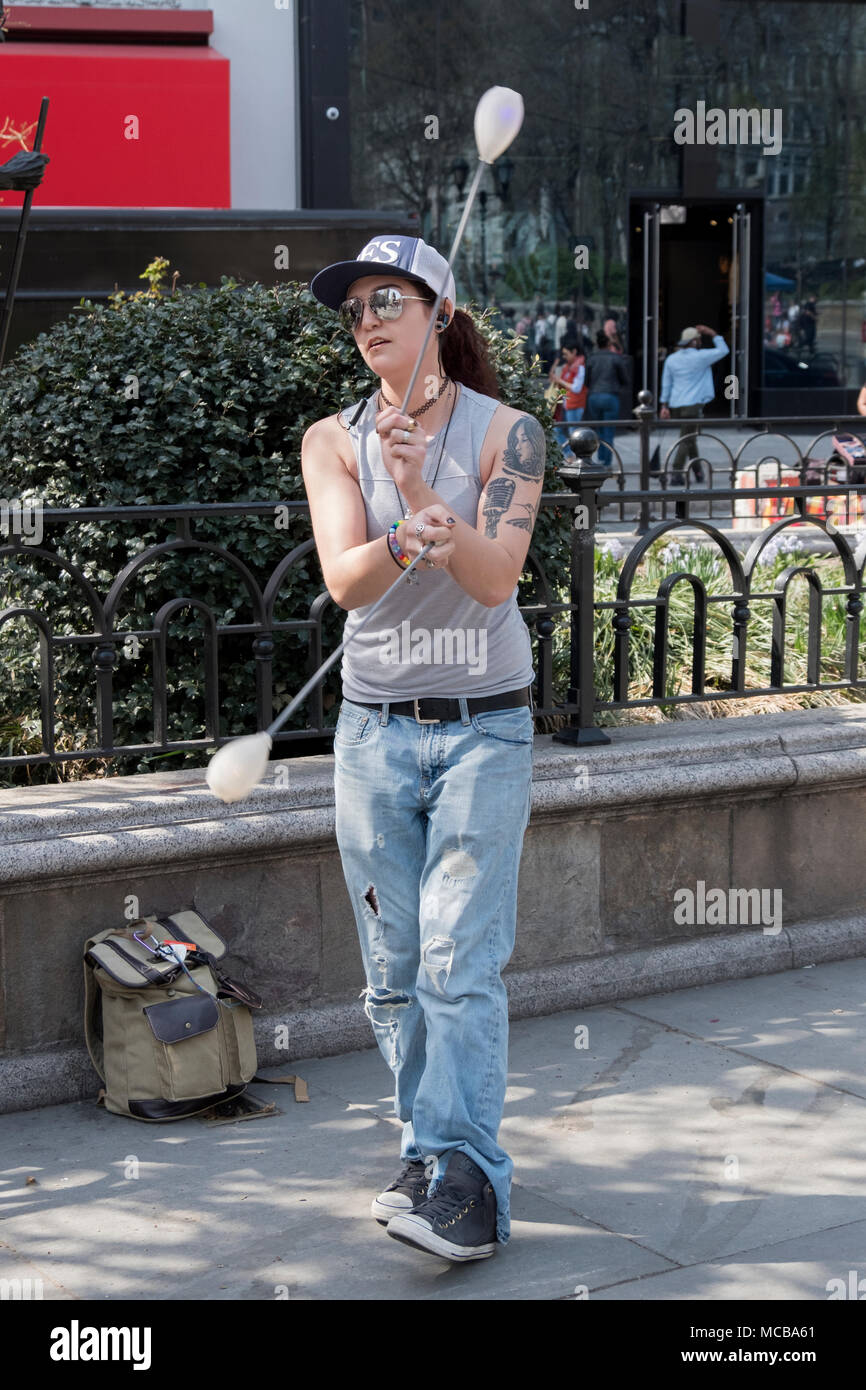 An attractive young lady performance artists performing POI - the swinging of tethered balls in rhythmic patters. In Union Square Park in New York. Stock Photo