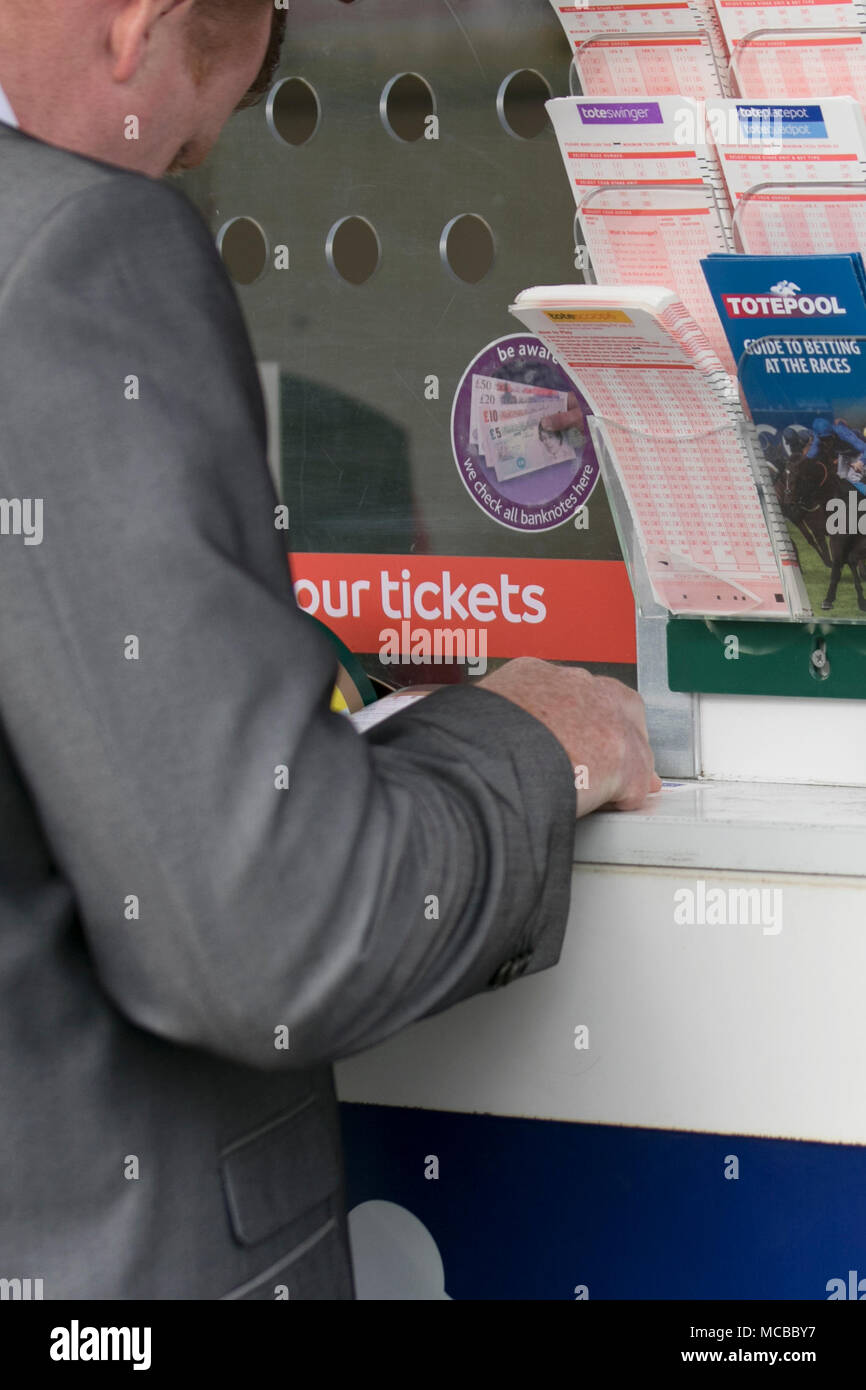 Man completing betting slip at TotePool, Liverpool, UK. Aintree Racecourse, bookmaker, crowd, gambling, horse racing, horses, loose, money, people, racecourse, race horse, track, jockey, gamble, racetrack, racegoer tourism in Liverpool, UK Stock Photo