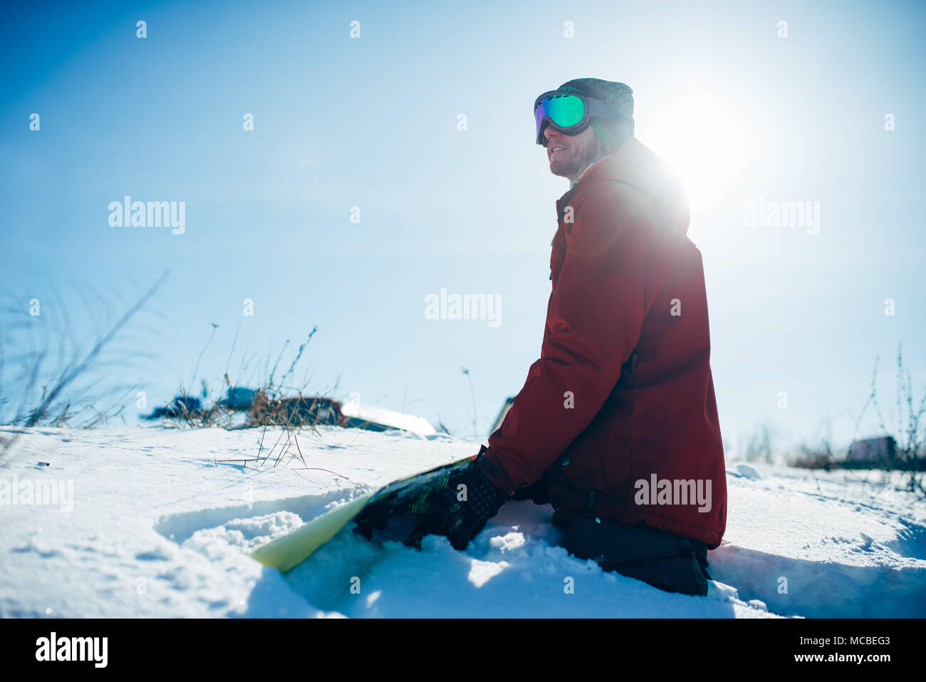 Snowboarder sitting on snowy slope in sunny day Stock Photo