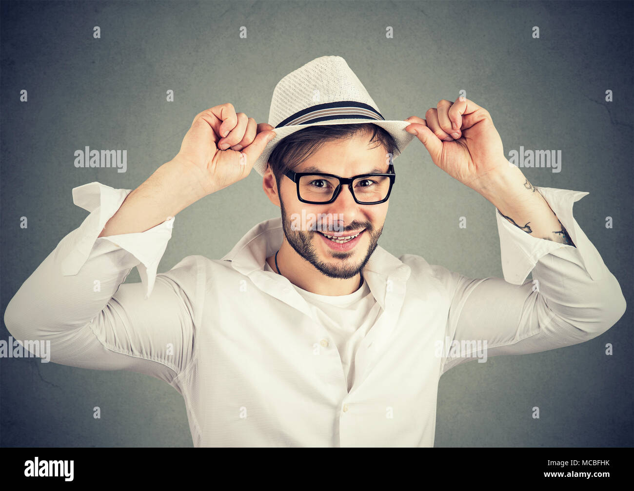 Handsome hipster man wearing trendy hat with eyeglasses smiling at camera on gray. Stock Photo