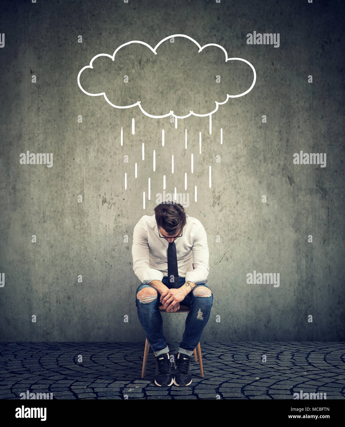 Sad casual businessman sitting on a chair looking down with a rain cloud above him Stock Photo