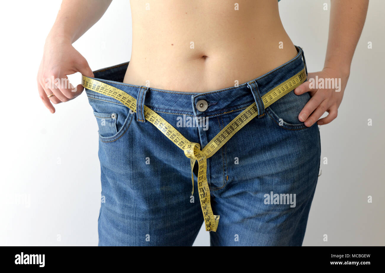 Weight loss concept. Woman shows her weight loss by wearing an old jeans. Healthy lifestyle, dieting concept with oversized jeans. Stock Photo