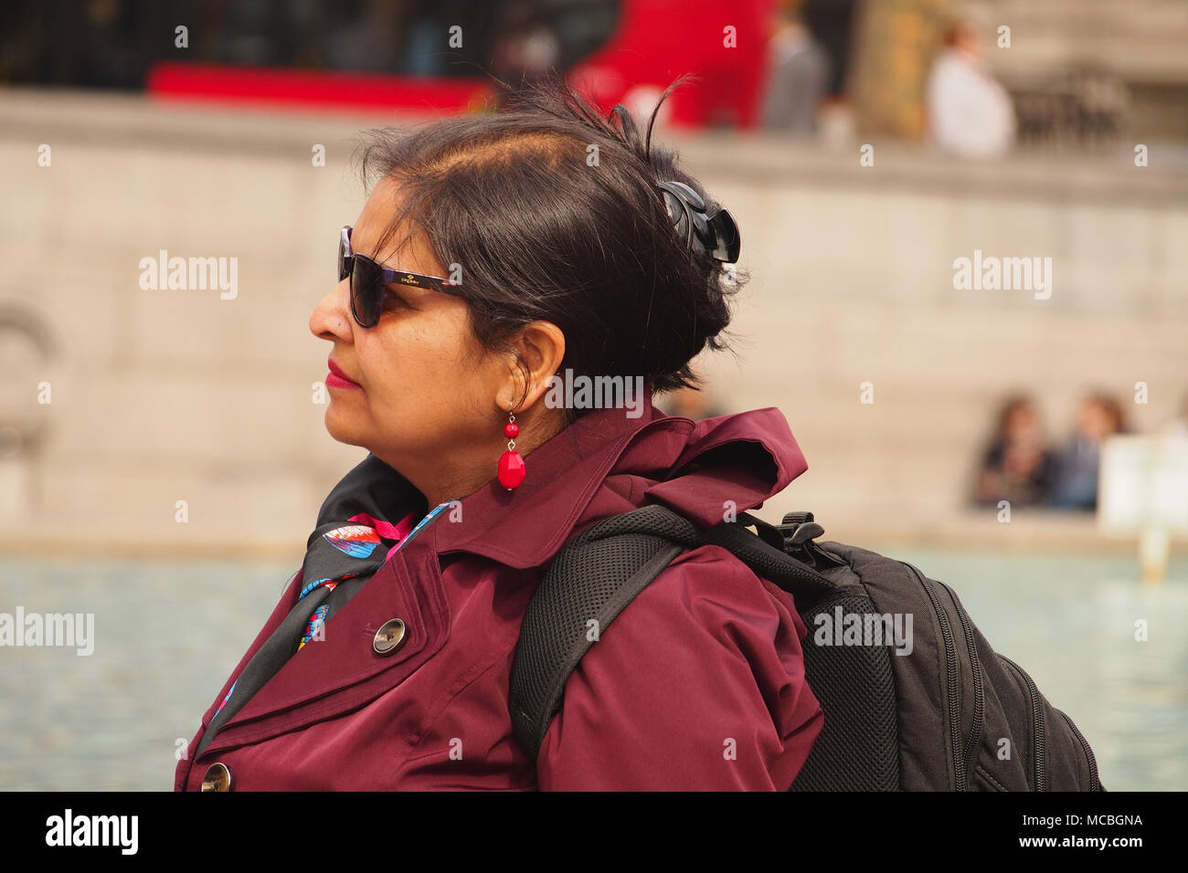 A woman sightseer in Trafalgar Square, London, taking in the sights on a bright winters day by the fountains Stock Photo