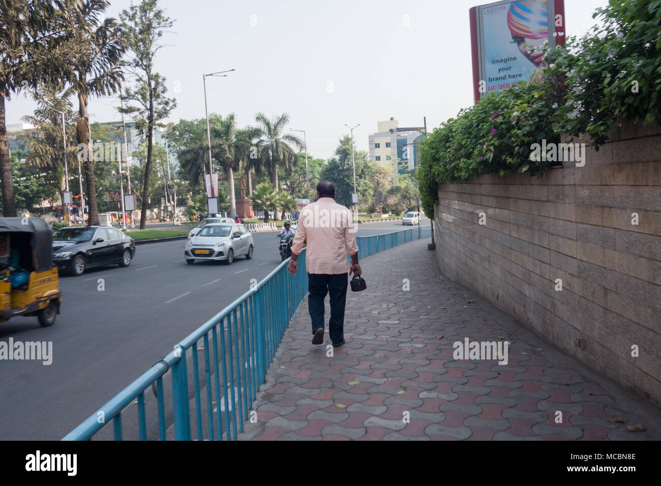 HYDERABAD, INDIA - APRIL 03,2018.A pedestrian with lunch box in hand walks on a pavement next to GVK Mall early morning in Hyderabad,India Stock Photo