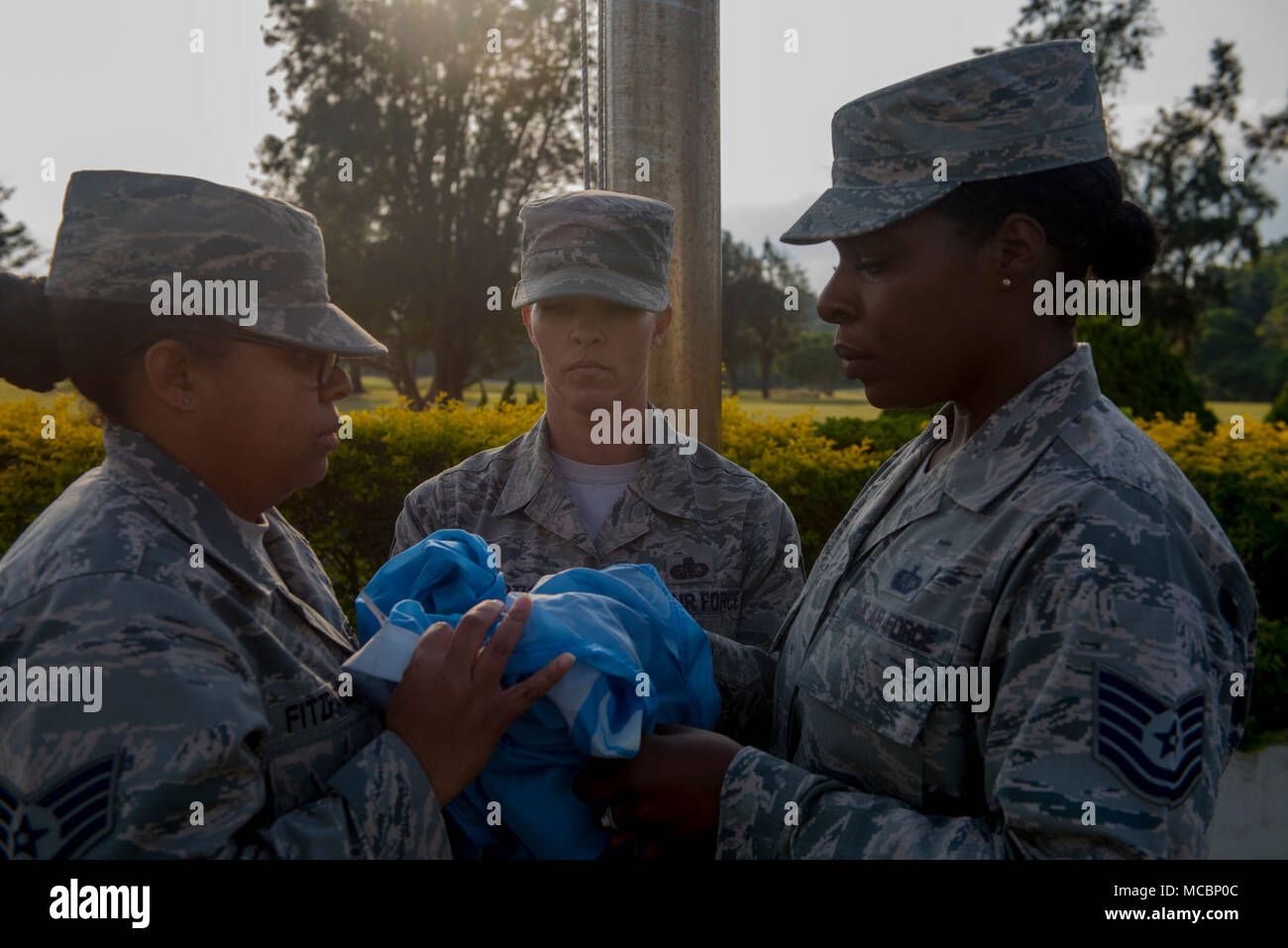 U.S. Air Force Staff Sgt. Charnay Fitzpatrick 18th Wing Professional Military Education Center administrative assistant, left, Chief Master Sgt. Tiffany Bettisworth, 18th Force Support Squadron superintendent, and Tech. Sgt. Patricia Gant, 18th FSS dinning facility manager, fold a United Nations flag during a retreat ceremony Mar. 30, 2018, on Kadena Air Base, Japan. Retreat is a long-standing tradition honoring the flag and signaling the end of the duty day. Stock Photo