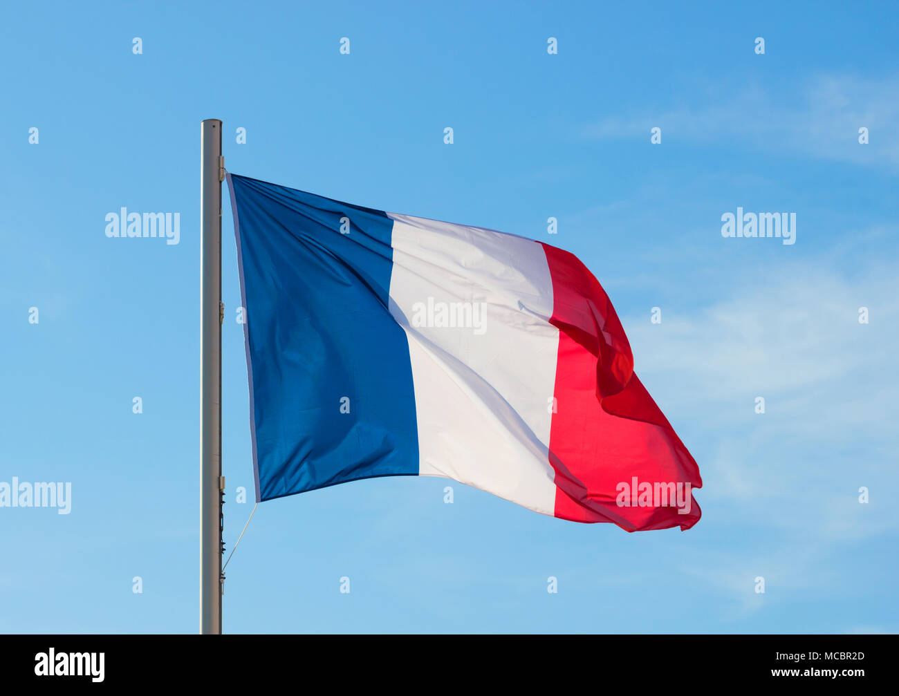 French flag fluttering in a brisk breeze against a bright blue sky in summer background. Stock Photo